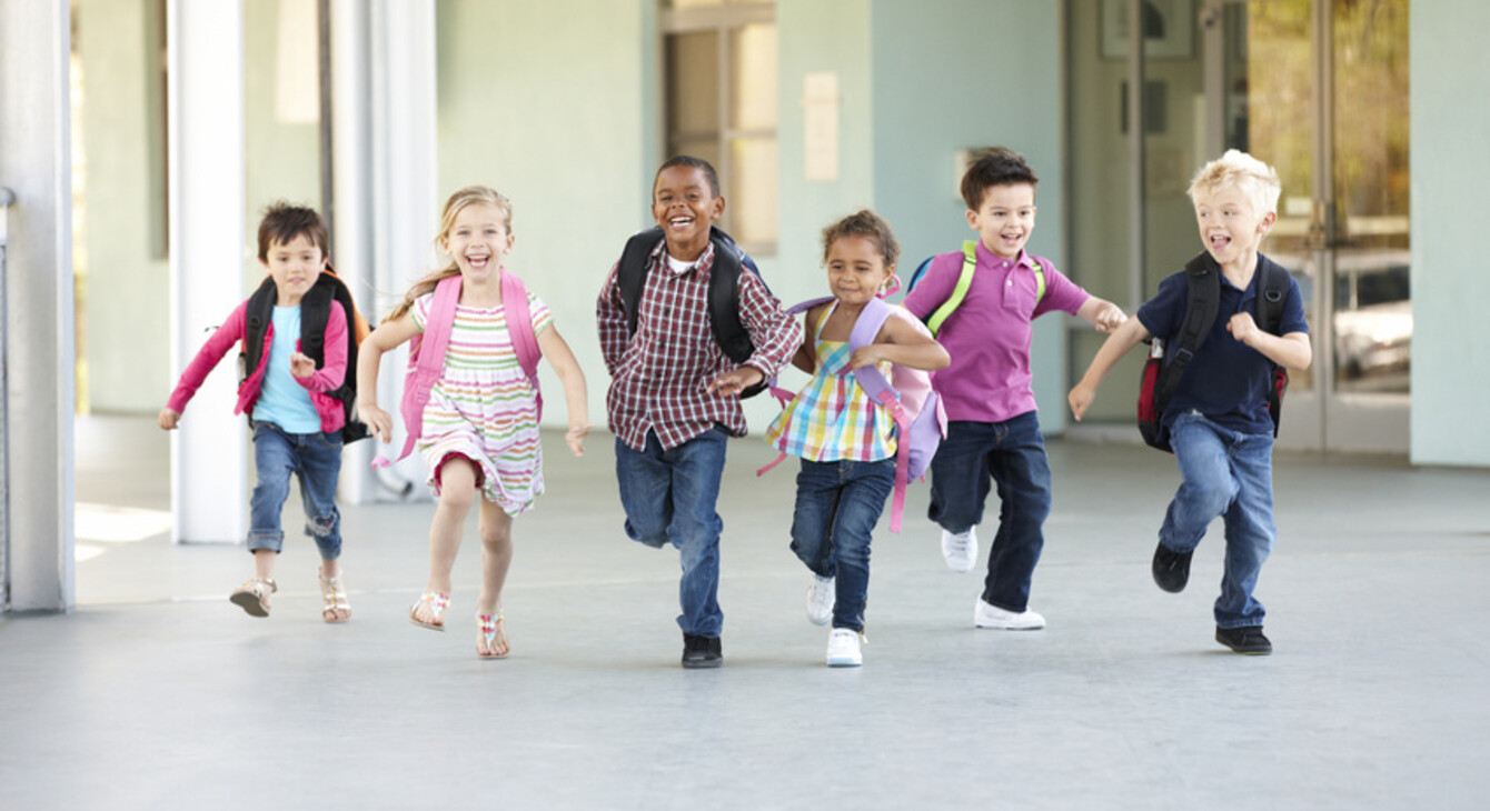 Six écoliers qui courent vers l'école tout sourire