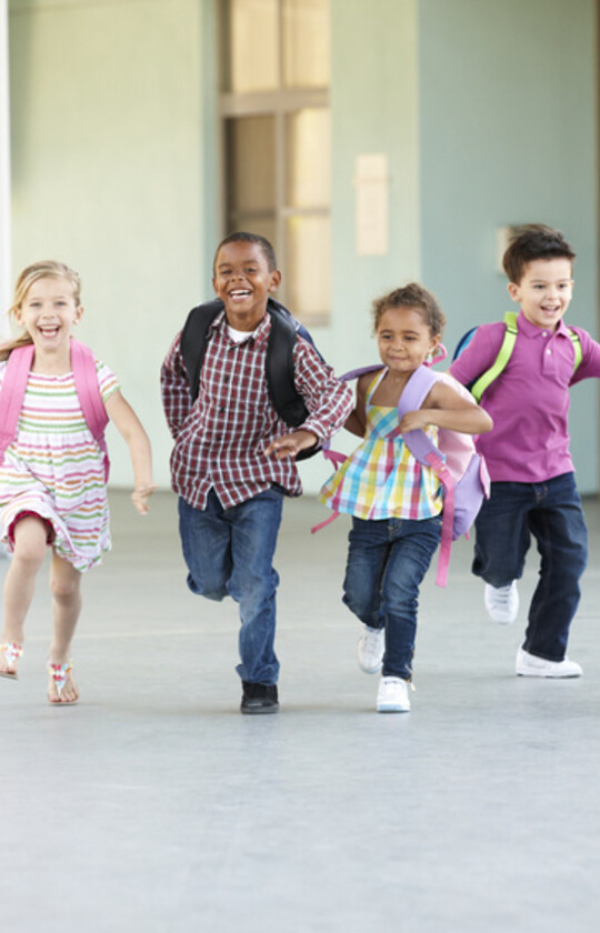 Six écoliers qui courent vers l'école tout sourire